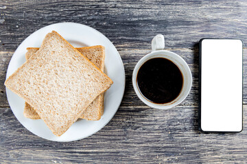 Sliced bread on the plate and cup of coffee with a mobile phone with a blank screen