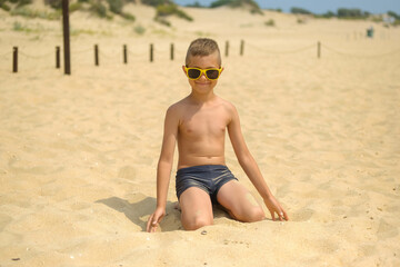 Little boy in sunglasses on the beach. Child in swimming trunks on the sea sand.