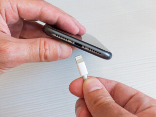 A man holds a smartphone charging cord connector in his hands next to the charging hole. Connect phone to charger.
