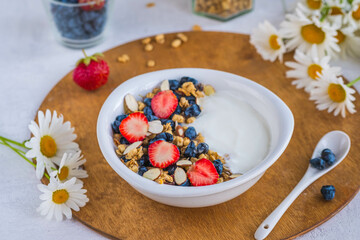 Unsweetened yogurt with granola, strawberries, honeysuckle and almond petals in a white bowl on a...