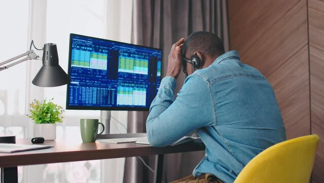 Back view portrait of african american trader in headphones being devastated and dissapointed after looking at trading charts. Crypto currency trader on falling market, stock failure concept. 4k.