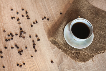 A cup of fragrant morning coffee stands on a saucer on a wooden brown table covered with a linen...