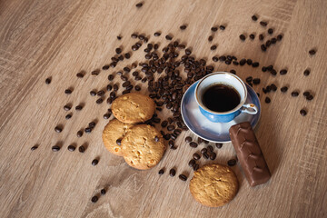 Roasted coffee beans and cup of coffee with drink on dark wooden surface, nearby lies chocolate and...