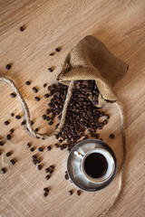 Roasted coffee beans in little bag with ropes and cup of coffee with drink on dark brown wooden...