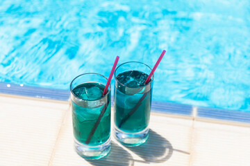 Chilled soft drinks, two blue cocktails with ice near the swimming pool in sunny day.
