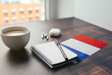 france national flag, notebook, pen, wireless headphones and coffee cup on wooden table during...