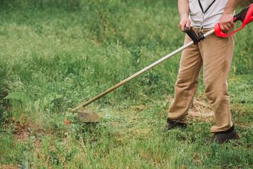 Man mowing lawn with electric trimmer in the garden. No face