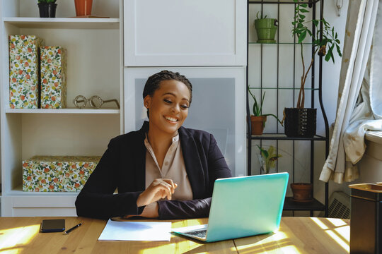 Smiling Young Adult Entrepreneur Freelance Black Woman Small Business Owner On Video Call With Laptop Working In Home Office Shot