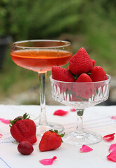Glass with cocktail and fresh strawberry on a garden table. Green tree leaves on a background. Summer day evening. 