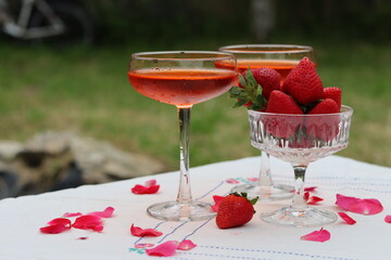 Glass with cocktail and fresh strawberry on a garden table. Green tree leaves on a background....