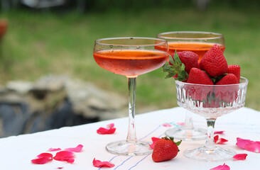 Spritz cocktails and fresh strawberry in a glass bowl. Picnic in the garden. Glass tableware close up photo. Rustic still life with seasonal fruit. 