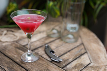 red cocktail with ice in glass with stem on wooden surface