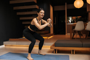 Athletic young caucasian woman doing pre-workout to warm up muscles on mat. Brunette wears black...