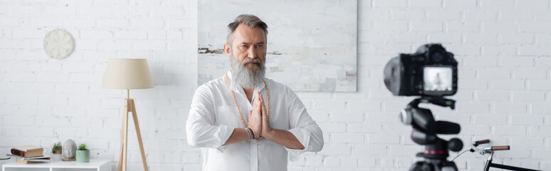 bearded guru man meditating with praying hands near digital camera, banner.
