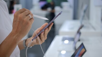 Close-up in the hands of the buyer a stylus and a tablet, touching the stylus to the screen of the tablet. A woman uses a stylus to check the screen of a graphics tablet. Ubud - Indonesia - 2022.