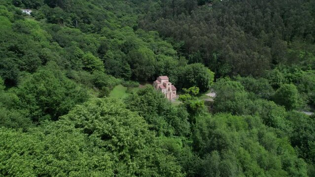 Droone flying towards ancient and roman church in green natural forest environment