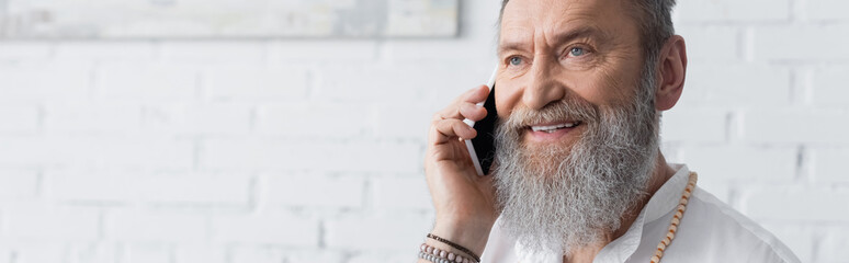 smiling bearded spiritual mentor talking on cellphone at home, banner.