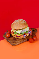 Delicious burger on the board with cutlet, tomatoes and cheese, cucumber and lettuce. On a red...