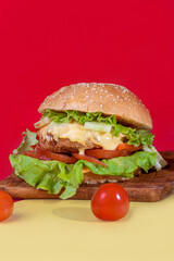 Delicious burger on the board with cutlet, tomatoes and cheese, cucumber and lettuce. On a red background. Fast food.