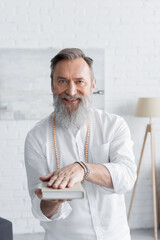 happy spiritual coach looking at camera while holding book.
