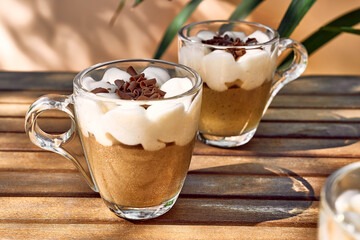 Traditional Italian dessert Tiramisu in glass cups on wooden table. National cuisine recipe. Summer refresh coffee cream sweet mousse dish.