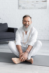 happy yoga coach in beaded bracelets sitting in easy pose and looking at camera.