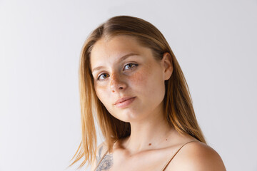 Close-up portrait of beautiful tender young girl with no makeup face isolated over grey studio background. Freckled beauty