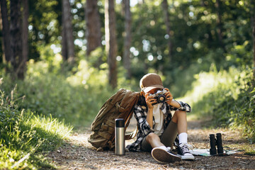 Girl traveler sitting on the road in woods and making photos on her camera