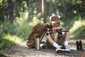 Girl traveler sitting on the road in woods and making photos on her camera