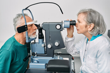 Optometrist doing sight test for senior man at modern ophthalmology clinic. Eye exam and vision diagnostic