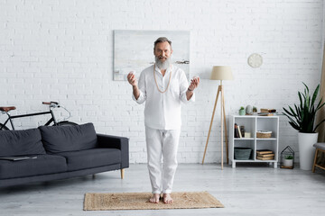 full length of yoga guru in white clothes standing with selenite stones at home.
