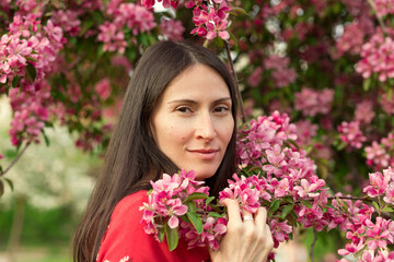 Fototapeta premium Portrait of a young woman among the flowering branches of apple trees in the spring garden.