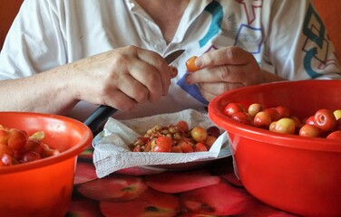 Hände von Frau mit Messer entkernen und entwurmen Kirschen am Tisch in Küche im Frühling