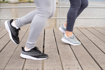 Cropped image of women jogging on embankment. Women in sportive clothes exercising on cloudy day. Sport, friendship concept