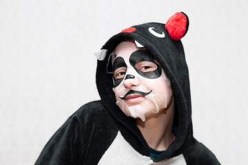 A young girl, a teenager in a kigurumi bat and a cosmetic mask on her face in the form of a panda...