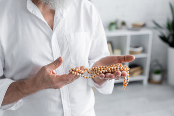 partial view of senior guru man in white shirt meditating with rosary.