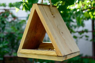 Small wooden birdhouse is hanging on a natural rope on the tree. Waiting for the birds. DIY birdhouse. Background picture.