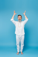 Fototapeta na wymiar full length of yoga master meditating with raised hands white standing on blue.