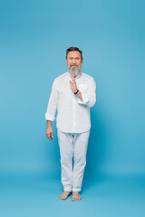 Fototapeta premium full length of master guru in white clothes showing blessing gesture on blue.
