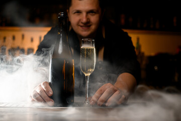 Selective focus on champagne glass with drink and bottle at smoked bar