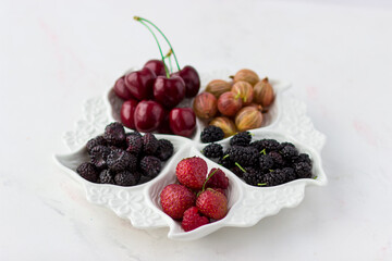 Berry plate on a white background. Strawberries, gooseberries, cherries, raspberries and mulberries