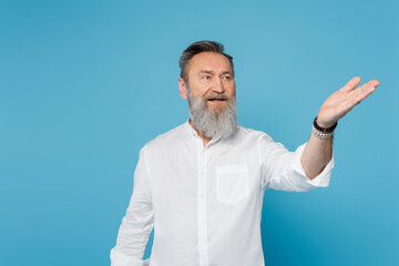 senior bearded guru man looking away and pointing with hand isolated on blue.