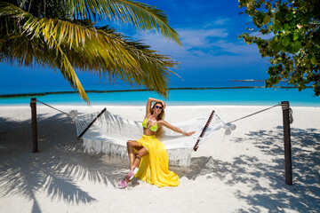 Elegant tanned woman in yellow swimsuit on tropical beach on Maldives island. Sexy female model...