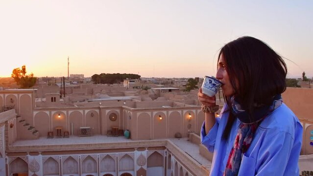 Yazd, Iran - 19th june, 2022: female caucasian person drink persian persian coffee from decorative cup in traditional rooftop cafe relax enjoy panoramic views of old town