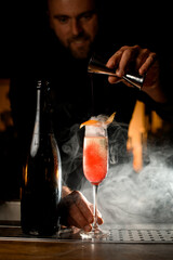 bottle and wineglass of smoked carbonated cocktail on the bar counter. Bartender pours liquid from a jigger into glass