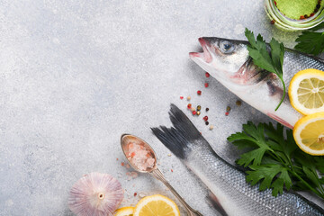 Fresh fish. Sea Bass raw with salt, pepper, parsley, olive oil and lemon on cutting board on light gray concrete rustic background. Food cooking background. Top view, copy space.