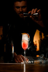 Focus on wineglass of smoked carbonated cocktail and male bartender pouring liquid from a jigger into glass