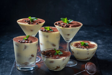 Traditional Italian dessert tiramisu decorated with cocoa powder, coffee beans and green mint on table, close up