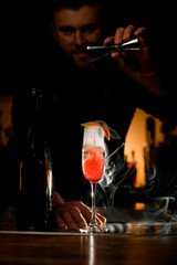 Beautiful wineglass of smoked carbonated cocktail and male bartender pouring liquid from a jigger into glass
