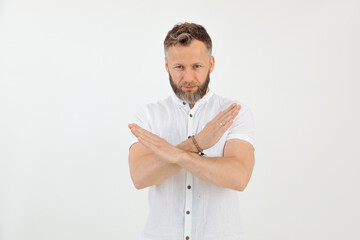 Bearded serious tattooed man negatively looking at camera in white outfit with crossed hands, deny,...